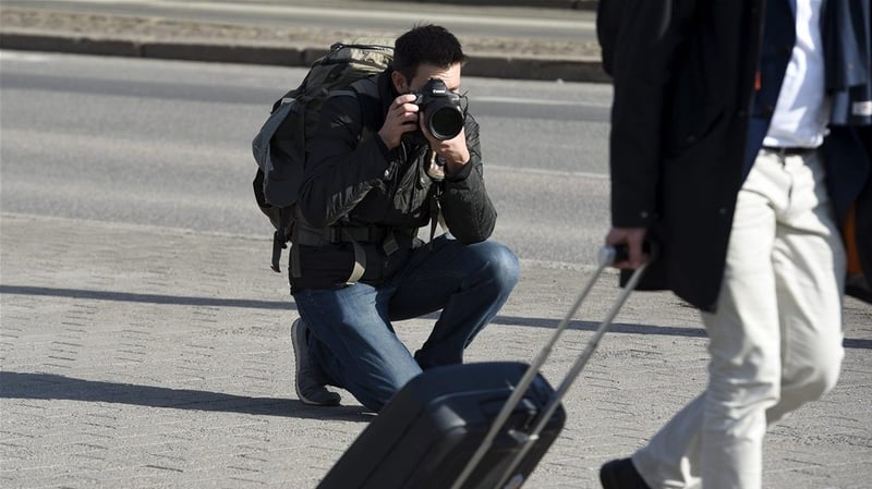 Valokuvaaja kuvaa matkalaukkua vetävää miestä